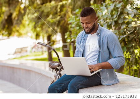 Handsome Black Freelancer Guy Working On Laptop In Park While Parked His Bike Near Bench Handsome Black Freelancer Guy Working On Laptop In Park While Parked His Bike Near Bench 125173938