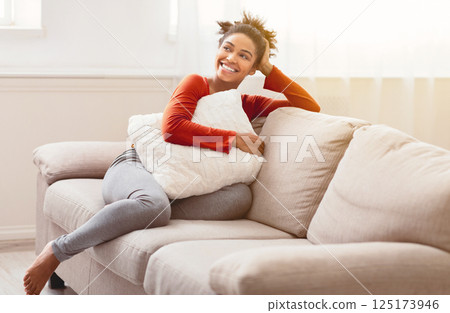 Weekend. Cheerful Black Girl Sitting On Couch Hugging Pillow Relaxing At Home On Weekend Morning. Empty Space 125173946