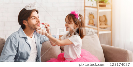 Cute little princess putting lipstick on her father. Young father enjoying time with child at home Cute little princess putting lipstick on her father. Young father enjoying time with child at home 125174027
