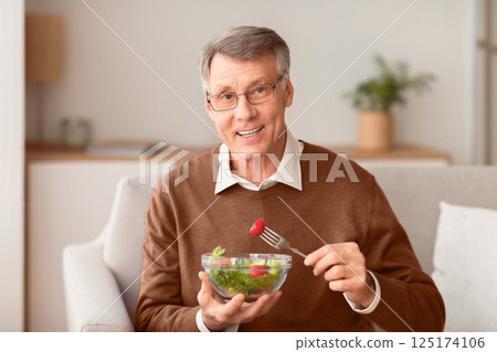 Healthy Nutrition. Senior Man Enjoying Vegetable Salad Smiling To Camera Sitting On Sofa At Home. Selective Focus Healthy Nutrition. Senior Man Enjoying Vegetable Salad Smiling To Camera Sitting On Sofa At Home. Selective Focus 125174106