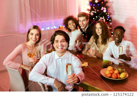 Happy New Year. Millennial Friends Holding Champagne Glasses Toasting Looking At Camera Sitting At Dinner Table At Home. Happy New Year. Millennial Friends Holding Champagne Glasses Toasting Looking At Camera Sitting At Dinner Table At Home. 125174122