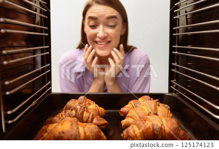 Homemade baking. Glad girl looking at tasty fresh croissants, view from inside of oven 125174123