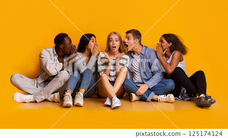 Shocked girl listening to her international classmates whispers, yellow background, panorama Shocked girl listening to her international classmates whispers, yellow background, panorama 125174124