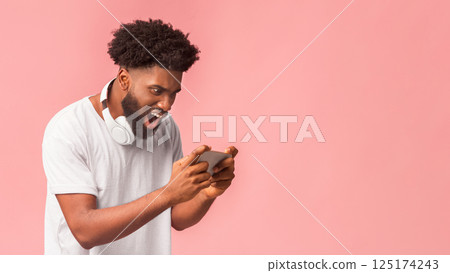 Phone crushed. Anxious black man looking at phone with angry face over pink background, wearing wireless headset, copy space Phone crushed. Anxious black man looking at phone with angry face over pink background, wearing wireless headset, copy space 125174243