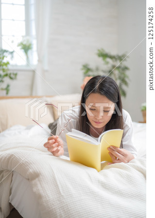 Beautiful woman reading in bed | Study | Hobby | Healthy living image | Well-being girl | Well-being 125174258