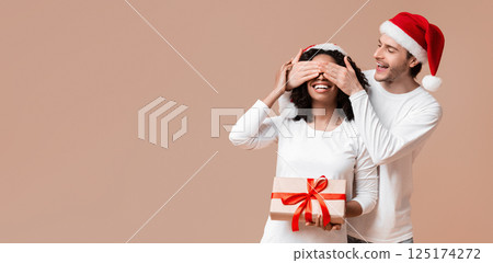 Romantic Boyfriend Covering Eyes of His Afro Girlfriend And Giving New Year Or Christmas Present, Making Surprise. Yellow Background With Free Space 125174272