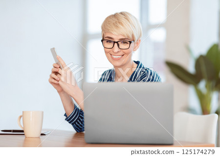 Business Application. Successful Businesswoman Using Smartphone Sitting At Laptop Computer In Modern Office. Selective Focus 125174279