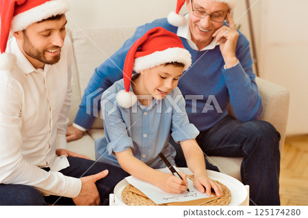 Christmas. Boy With Father And Grandpa Writing Letter To Santa Claus Sitting Together On Couch At Home. Selective Focus 125174280