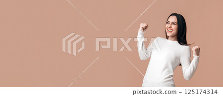 Yes, I did it. Euphoric brunette girl celebrating success with raised fists, rejoicing victory or personal achievement over yellow background, panorama 125174314