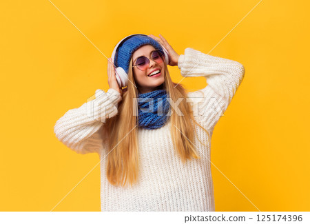 Joyful young winter girl in wireless headphones listening to music and dancing over pink background 125174396