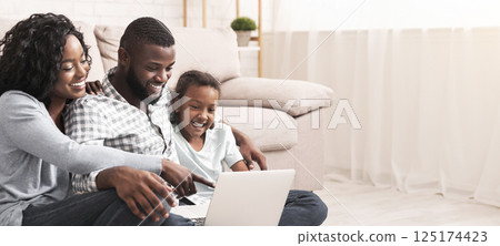 Joyful african american family of three using laptop at home together, watching movie or browsing internet Joyful african american family of three using laptop at home together, watching movie or browsing internet 125174423