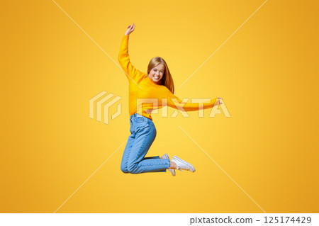 Forever young. Joyful teen girl jumping in air on orange background with copy space 125174429