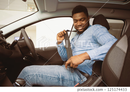 Own Car. African American Man Putting On Seat Belt Sitting In Auto In Dealership Store. Selective Focus Own Car. African American Man Putting On Seat Belt Sitting In Auto In Dealership Store. Selective Focus 125174433