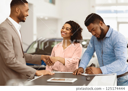 Buying Car. Black Couple Shaking Hands With Salesman And Signing Papers In Cars Selling Center. Selective Focus 125174444