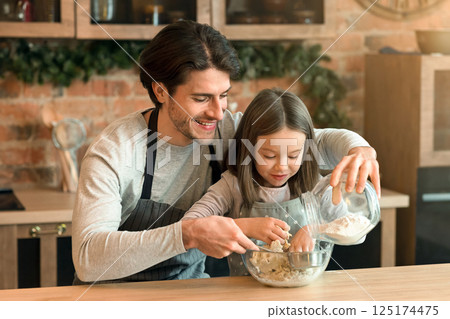 Happy father and daughter baking cookies, kneading dough together, adding flour and having fun in kitchen, free space 125174475