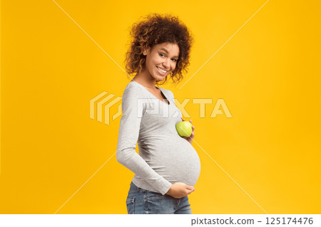 Healthy nutrition. Happy expectant woman holding apple and touching belly over pink background 125174476