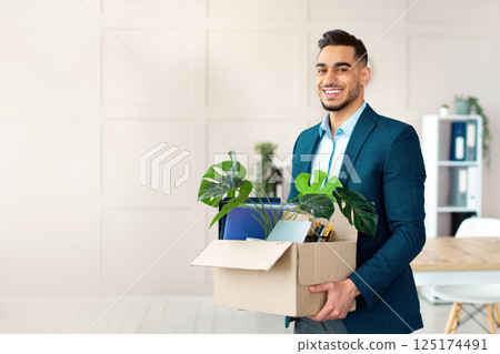 First day at office. Portrait of confident Arab businessman with belongings moving to new office. Happy young guy manager holding box with supplies, changing working place, indoors First day at office. Portrait of confident Arab businessman with belongings moving to new office. Happy young guy manager holding box with supplies, changing working place, indoors 125174491