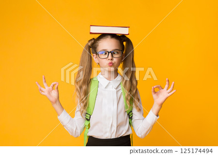 Back To School Concept. Cute Nerdy Schoolgirl Meditating With Book On Head On Yellow Studio Background. Free Space Back To School Concept. Cute Nerdy Schoolgirl Meditating With Book On Head On Yellow Studio Background. Free Space 125174494