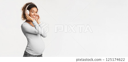 Pregnancy and motherhood concept. Black pregnant woman listening music in headphones, white background 125174622