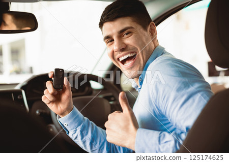 Happy Man Showing New Car Key To Camera Gesturing Thumbs Up Sitting In Auto In Dealership Store Happy Man Showing New Car Key To Camera Gesturing Thumbs Up Sitting In Auto In Dealership Store 125174625
