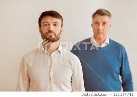 Serious Middle Aged Son And His Elderly Father Standing Looking At Camera On White Background. Selective Focus 125174711