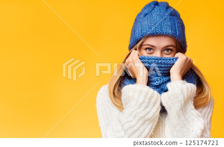 Enigmatic blonde girl hiding from winter cold over pink background, covering face with scarf, free space 125174721