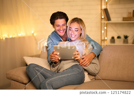 Happy young couple using tablet and enjoying time together at cozy winter evening 125174822
