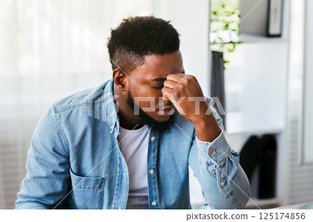Exhausted african american employee massaging his nose bridge, tired of long time work in office, copy space Exhausted african american employee massaging his nose bridge, tired of long time work in office, copy space 125174856