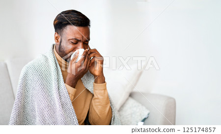 Seasonal Flu. Sick Black Guy Calling Doctor And Blowing Nose In Paper Tissue Sitting On Sofa At Home. Free Space 125174857