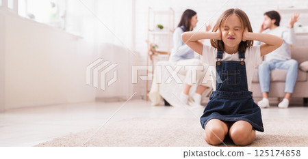 Little girl sitting on floor and covering ears with hands, tired of mom and dad arguing, quarrelling parents on background, selective focus on child Little girl sitting on floor and covering ears with hands, tired of mom and dad arguing, quarrelling parents on background, selective focus on child 125174858
