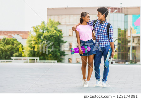 A teen African American couple walk side-by-side on a paved city street. They both hold skateboards. Guy has his arm around the girl, and they are looking at each other, copy space A teen African American couple walk side-by-side on a paved city street. They both hold skateboards. Guy has his arm around the girl, and they are looking at each other, copy space 125174881