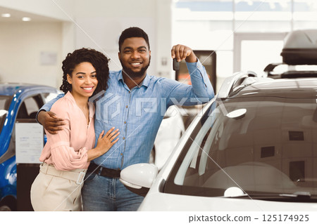 Cheerful African Spouses Holding Car Key Standing Near New Family Automobile In Dealership Center. Copy Space Cheerful African Spouses Holding Car Key Standing Near New Family Automobile In Dealership Center. Copy Space 125174925