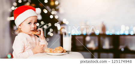 Christmas brunch. Baby girl eating cookie with milk near xmas tree, free space Christmas brunch. Baby girl eating cookie with milk near xmas tree, free space 125174948