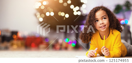 Pensive cute little afro girl thinking about gift ask from Santa, lying on floor at home, empty space 125174955