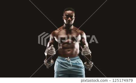 A muscular man lifts dumbbells while looking intensely at the camera. A muscular man lifts dumbbells while looking intensely at the camera. 125174979