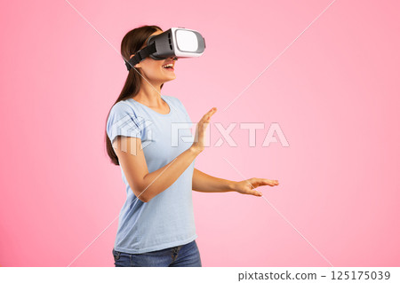 Excited woman using VR headset and experiencing virtual reality, yellow studio wall 125175039