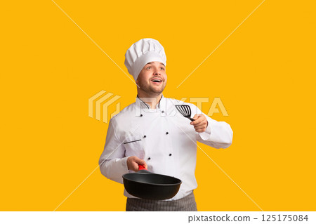 Excited Chef Cook Guy Holding Pan Throwing Invisible Food Looking Up Standing Over Yellow Background. Studio Shot, Empty Space 125175084