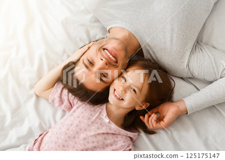 Top view of handsome young father and his cute little daughter looking at camera and smiling, lying on bed at home, just woke up, affectionate concept Top view of handsome young father and his cute little daughter looking at camera and smiling, lying on bed at home, just woke up, affectionate concept 125175147