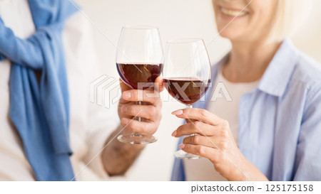 Mature couple clinking glasses of red wine, celebrating anniversary at home 125175158