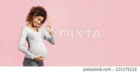 Easy pregnancy. Afro pregnant lady showing okay gesture and touching belly, pink background Easy pregnancy. Afro pregnant lady showing okay gesture and touching belly, pink background 125175218