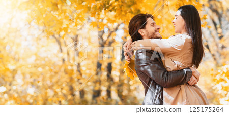 Cheerful guy lifting his happy girlfriend up, spending time together at autumn forest, panorama with copy space 125175264
