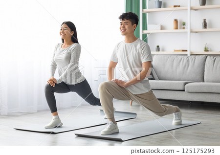 Motivated asian young couple exercising together at home, positive korean man and woman in sportswear standing on fitness mat, stretching and smiling, copy space. Healthy lifestyle concept Motivated asian young couple exercising together at home, positive korean man and woman in sportswear standing on fitness mat, stretching and smiling, copy space. Healthy lifestyle concept 125175293