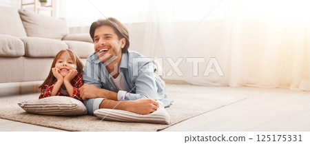 Happy family father and little daughter watching cartoons, lying on floor at home, free space 125175331