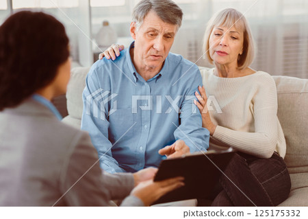 Last Will And Testament. Senior man sitting on couch with wife, checking document, signing papers with consultant Last Will And Testament. Senior man sitting on couch with wife, checking document, signing papers with consultant 125175332