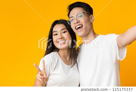 Cute asian couple in love taking selfie over yellow studio background, copy space Cute asian couple in love taking selfie over yellow studio background, copy space 125175337