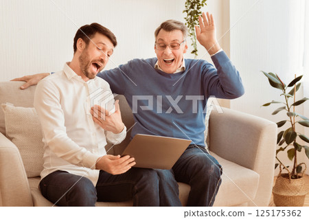 Relationship With Aging Parents. Mature Man And Senior Father Using Laptop Watching Old Photos Laughing Sitting On Couch Indoor. 125175362