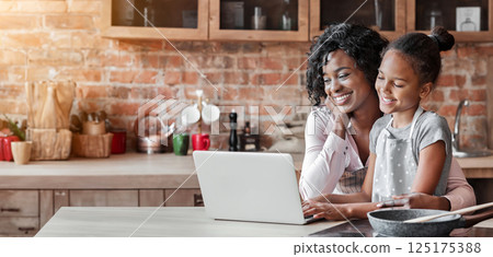 Black woman and her cute daughter reading recipe on laptop, cooking at kitchen, copy space 125175388