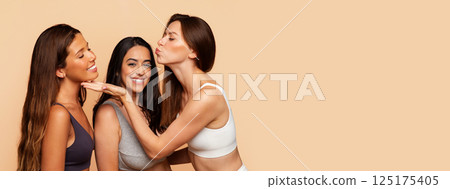 Three multiracial millennial women in underwear make air kissing, smiling, have fun, enjoy beauty care procedures on beige background. Health care and friendship, support, copy space Three multiracial millennial women in underwear make air kissing, smiling, have fun, enjoy beauty care procedures on beige background. Health care and friendship, support, copy space 125175405