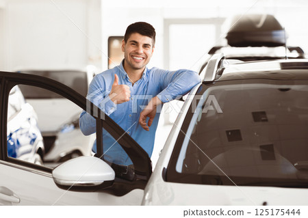 Great Car. Cheerful Guy Standing Near Auto Gesturing Thumbs Up Buying Vehicle In Dealership Center. Free Space 125175444