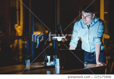 Young Businessman Working On Laptop Standing In Modern Office Late At Night. Business Lifestyle. Copy Space Young Businessman Working On Laptop Standing In Modern Office Late At Night. Business Lifestyle. Copy Space 125175606